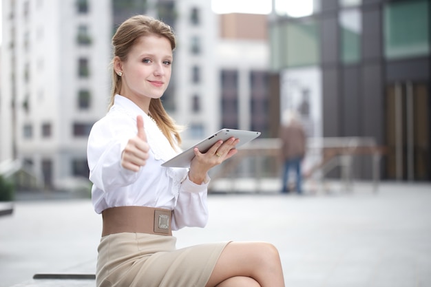 Femme d'affaires travaillant à l'extérieur de l'immeuble de bureaux avec des appareils numériques