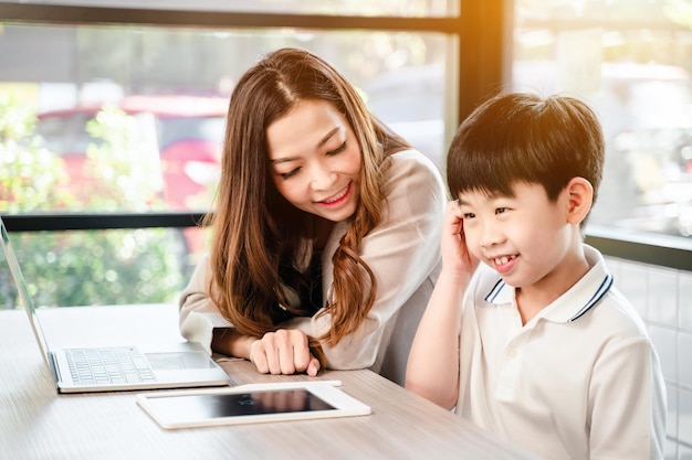 Femme d'affaires travaillant en ligne dans un café avec un enfant. Mode de vie familial asiatique avec téléphone portable et tablette numérique.