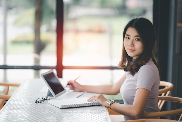 femme d'affaires travaillant sur un ordinateur portable et utilisant un stylo faisant des avis dans son cahier sur une table en bois avec une tasse de café. Notion d'entreprise