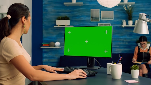 Femme d'affaires travaillant sur la publicité en ligne à l'aide d'un ordinateur avec une maquette d'affichage à clé chroma sur écran vert assis sur un bureau