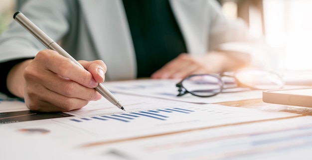 Femme d'affaires travaillant à son bureau dans le bureau vérifiant et analysant le rapport. Jeune femme d'affaires travaillant sur des graphiques de paperasse et de statistiques.