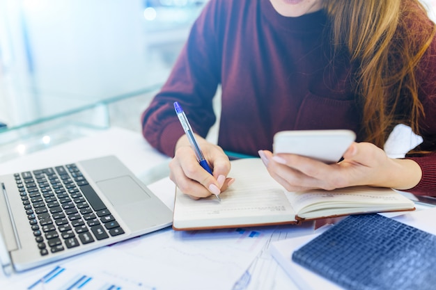 Femme d'affaires travaille à domicile, travail à distance à domicile, avec ordinateur portable et ordinateur portable, prend des notes sur le téléphone