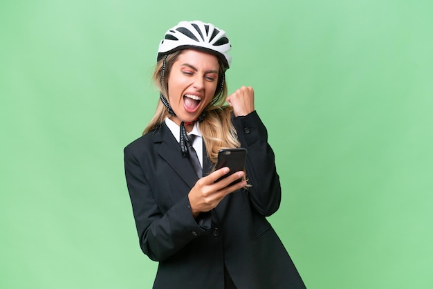 Femme d'affaires uruguayenne portant un casque de motard sur fond isolé avec téléphone en position de victoire