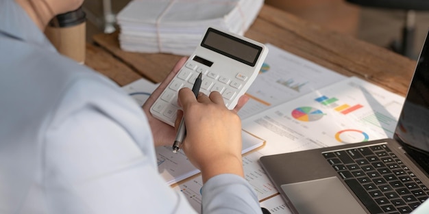 Femme d'affaires utilisant une calculatrice pour calculer le rapport financier travaillant au bureau avec un ordinateur portable sur la table Femme asiatique comptable ou banquier faisant des calculs finances et concept d'économie