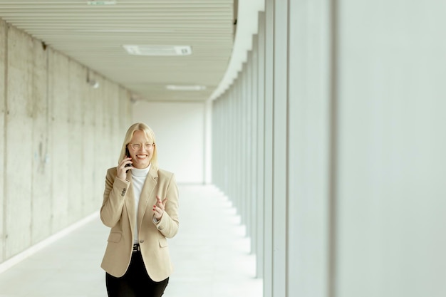 Femme d'affaires utilisant un téléphone portable dans un couloir de bureau moderne