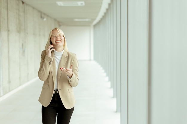 Femme d'affaires utilisant un téléphone portable dans un couloir de bureau moderne