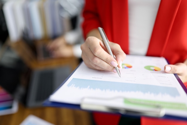 Femme d'affaires en veste rouge détient le presse-papiers avec des documents et un stylo agrandi. Maintenir le concept de documentation du personnel.