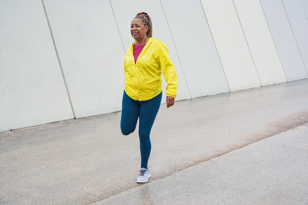 Femme africaine âgée faisant de l'exercice d'étirement sportif dans la ville pendant les jours de pluie