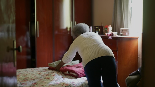 Photo une femme africaine âgée rangeant la chambre enlevant les vêtements du lit organisant les travaux ménagers