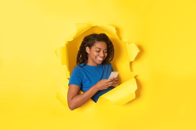 Femme africaine à l'aide de SMS de téléphone portable posant dans du papier jaune déchiré