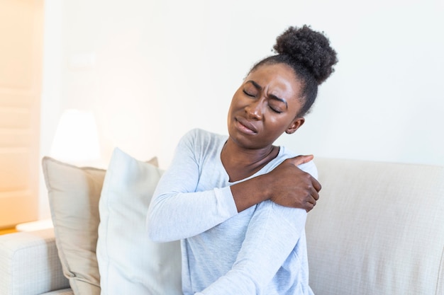 Photo femme africaine assise sur le canapé prendre une pause touche son épaule souffre de douleurs douloureuses causées par une mauvaise posture