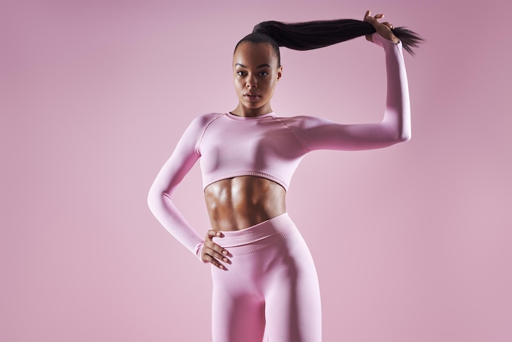 Photo une femme africaine attrayante en vêtements de sport ajustant ses cheveux sur un fond rose