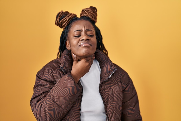 Femme africaine aux cheveux tressés debout sur fond jaune touchant le cou douloureux mal de gorge pour la grippe et l'infection