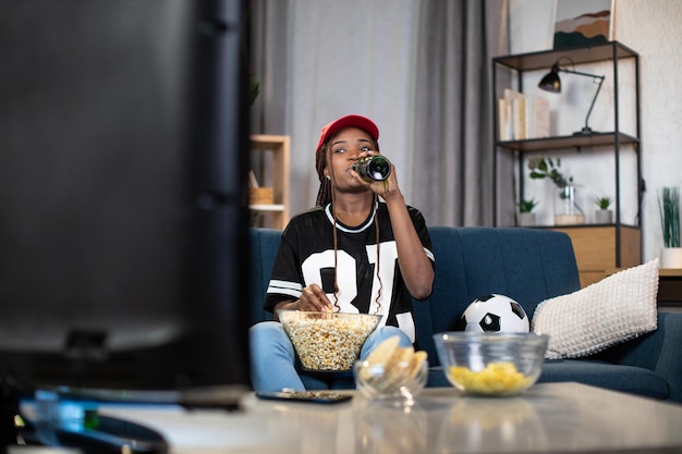 Femme africaine avec de la bière et des collations en regardant un match de football