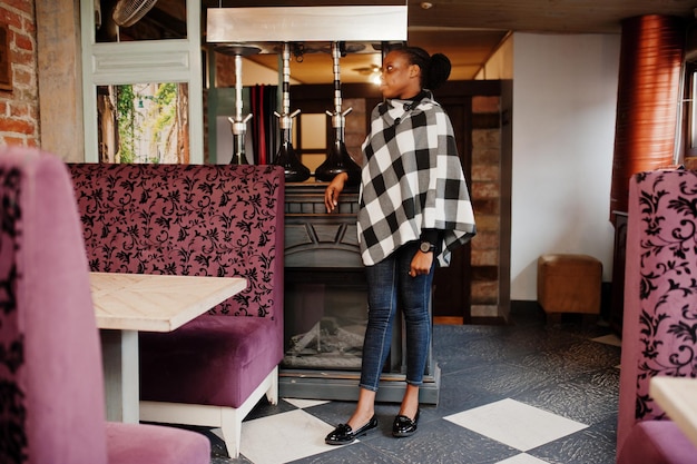 Femme africaine en cape à carreaux posée au café