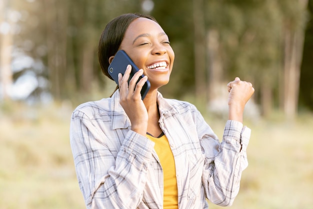 Une femme africaine célèbre et poing avec un appel téléphonique en plein air ou sourit pour gagner un succès ou un objectif en été Conversation d'aventure sur smartphone ou bonne nouvelle pour une fille dans la forêt ensoleillée ou la célébration