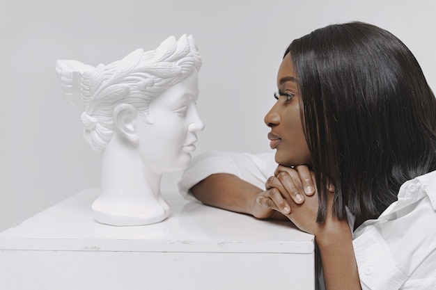 Femme africaine dans un studio. Mur blanc. Femme en chemise blanche.