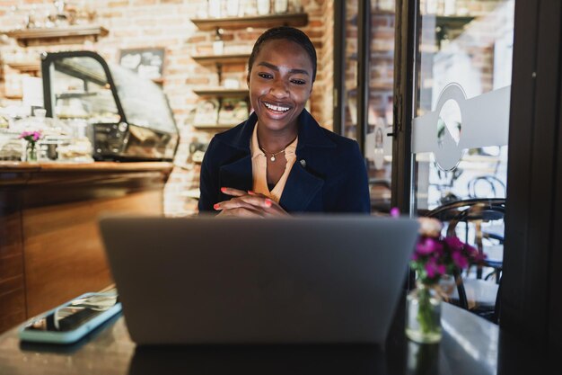 Une femme africaine fait un appel vidéo sur un ordinateur portable alors qu'elle est assise dans un café.