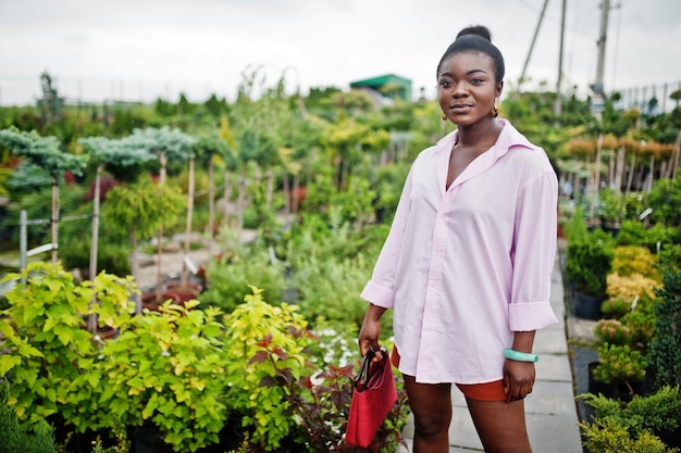 Femme africaine en grande chemise rose posée au jardin avec des semis