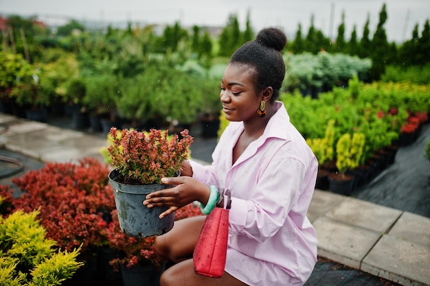 Femme africaine en grande chemise rose posée au jardin avec des semis