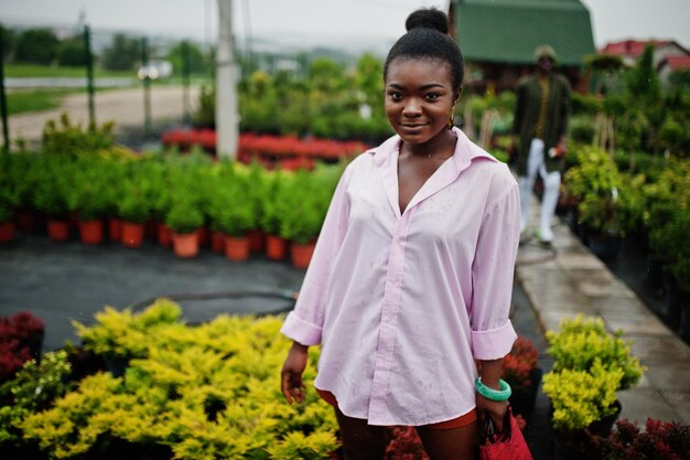 Femme africaine en grande chemise rose posée au jardin avec des semis