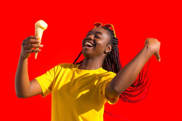 Une femme africaine heureuse tenant de la crème glacée et s'arrangant les cheveux.