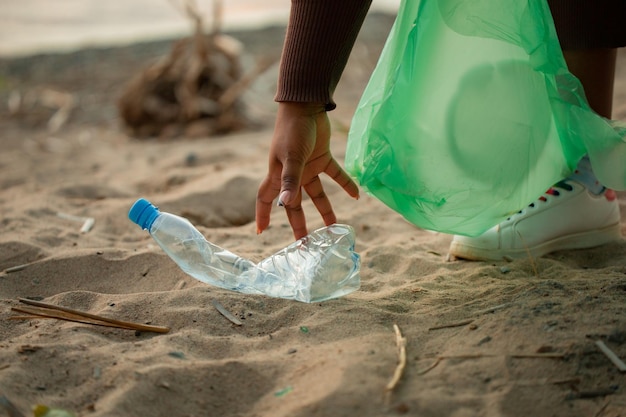 Femme Africaine Méconnaissable Se Penchant Pour Ramasser Les Déchets Du Sable Sur La Plage Dans Un Sac En Plastique Vert Pollution écologique