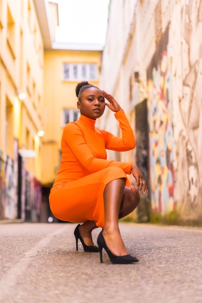 Femme africaine noire dans une robe orange et talons noirs sur une rue de la ville