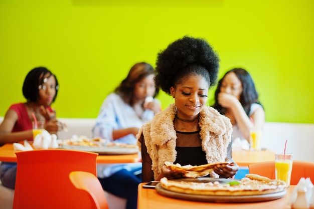 Femme africaine avec pizza assis au restaurant contre des filles à la peau foncée