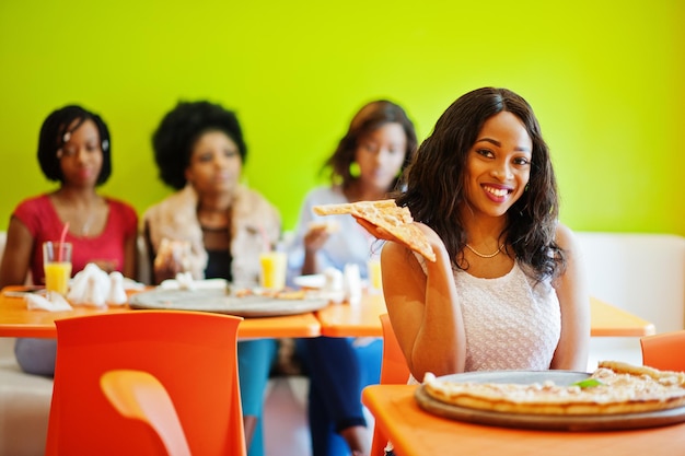 Femme africaine avec pizza assis au restaurant contre des filles à la peau foncée