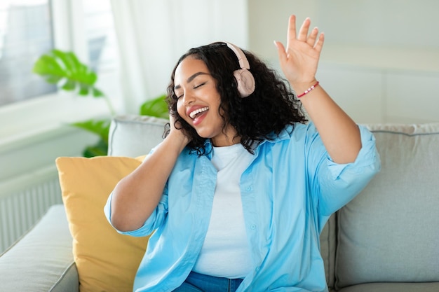 Femme africaine portant des écouteurs chantant avec les yeux fermés à la maison