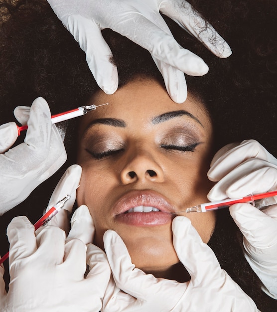 Femme africaine recevant une injection cosmétique de botox dans ses lèvres. Soins de beauté