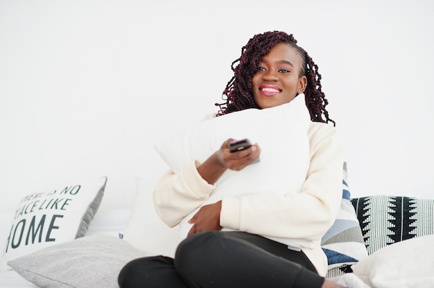 Femme africaine regardant la télévision à la maison et tenant une télécommande sur le lit