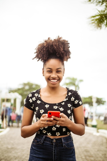 Femme africaine riant à l'aide d'un smartphone en regardant la caméra