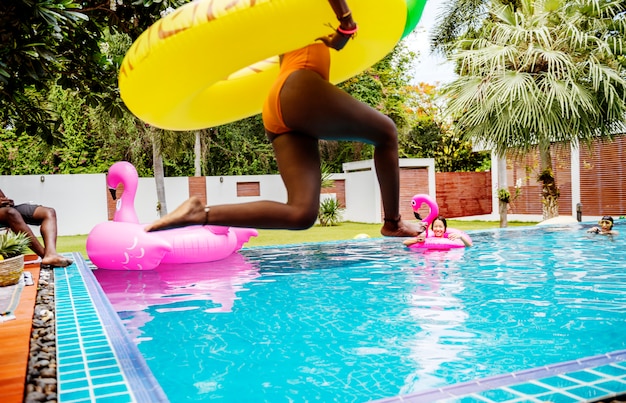 Une femme africaine sautant dans la piscine avec un flotteur gonflable et profitant de l’été