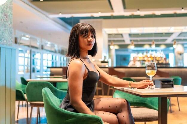 Une femme africaine sensuelle buvant du vin dans un restaurant de luxe.