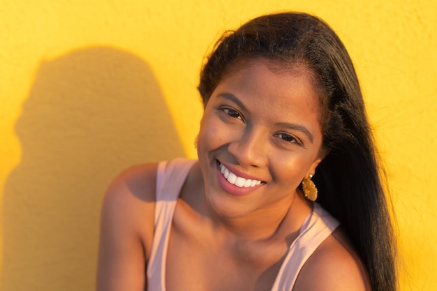 Femme africaine souriante debout au sommet d'un mur jaune regardant la caméra