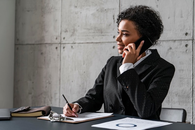 Femme africaine souriante parlant au téléphone et écrivant