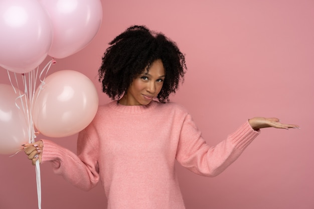 Femme africaine tenant beaucoup de ballons bénéficie d'une fête cool porte un pull rose fête son anniversaire