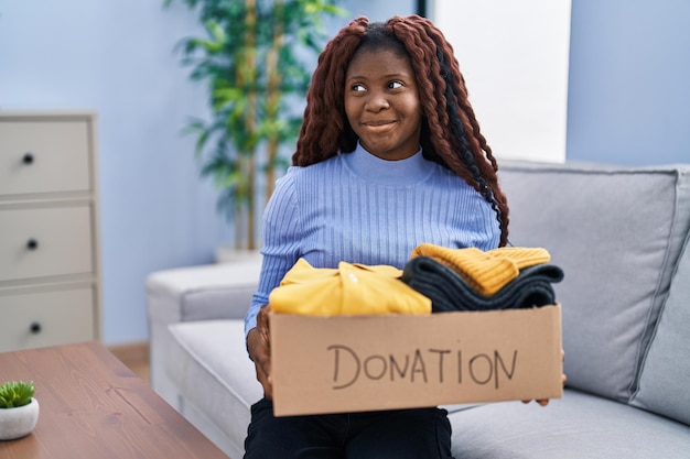 Femme africaine tenant une boîte de dons pour la charité souriante regardant sur le côté et regardant de côté en pensant.