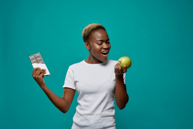 Femme africaine tenant une pomme et une barre de chocolat noir.