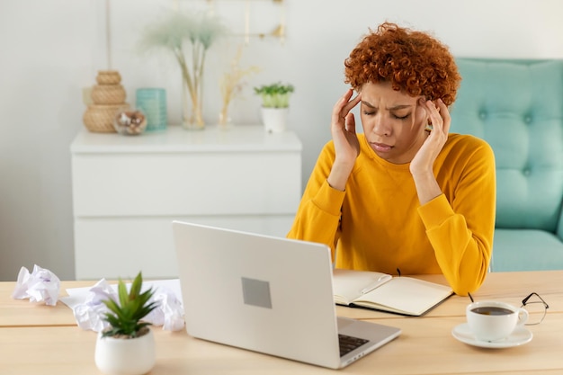 Femme africaine touchant les tempes en situation de stress Fille au bureau à domicile fatiguée de travailler se sentant mal à la tête malade se frottant les tempes front Longue utilisation d'un ordinateur portable Syndrome de vision par ordinateur Syndrome de bureau