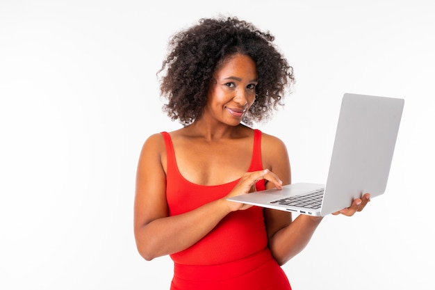 Femme africaine travaille avec ordinateur portable et sourires, photo isolée sur mur blanc