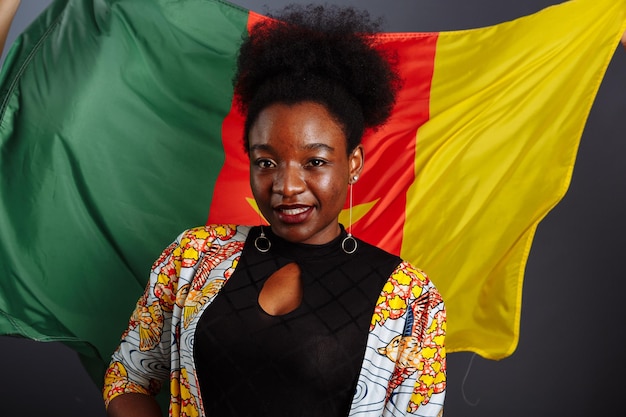 Photo femme africaine en vêtements nationaux posant et dansant contre le drapeau du cameroun