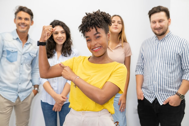 Femme afro d'affaires montrant les muscles des bras souriant fier. compagnons derrière