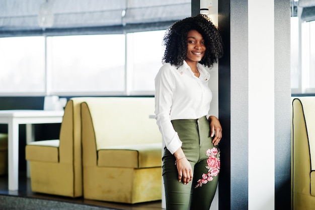 Une femme afro-américaine d'affaires pure avec des cheveux afro porte un chemisier blanc et un pantalon vert posés dans un café