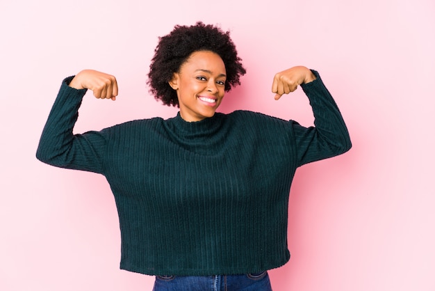 Femme afro-américaine d'âge moyen contre un mur rose isolé montrant un geste de force avec les bras, symbole du pouvoir féminin