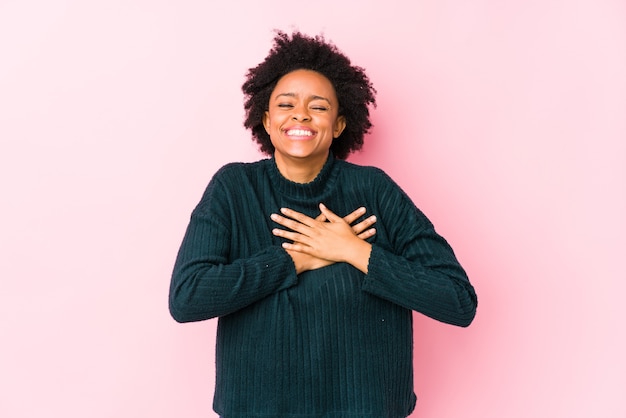 Femme afro-américaine d'âge moyen contre un rire isolé rose en gardant les mains sur le cœur, concept de bonheur.