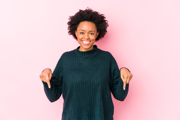 Femme afro-américaine d'âge moyen contre une surface rose isolé pointe vers le bas avec les doigts, sentiment positif.