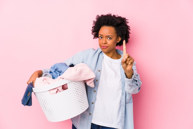 Femme afro-américaine d'âge moyen faisant la lessive isolé montrant le numéro un avec le doigt.